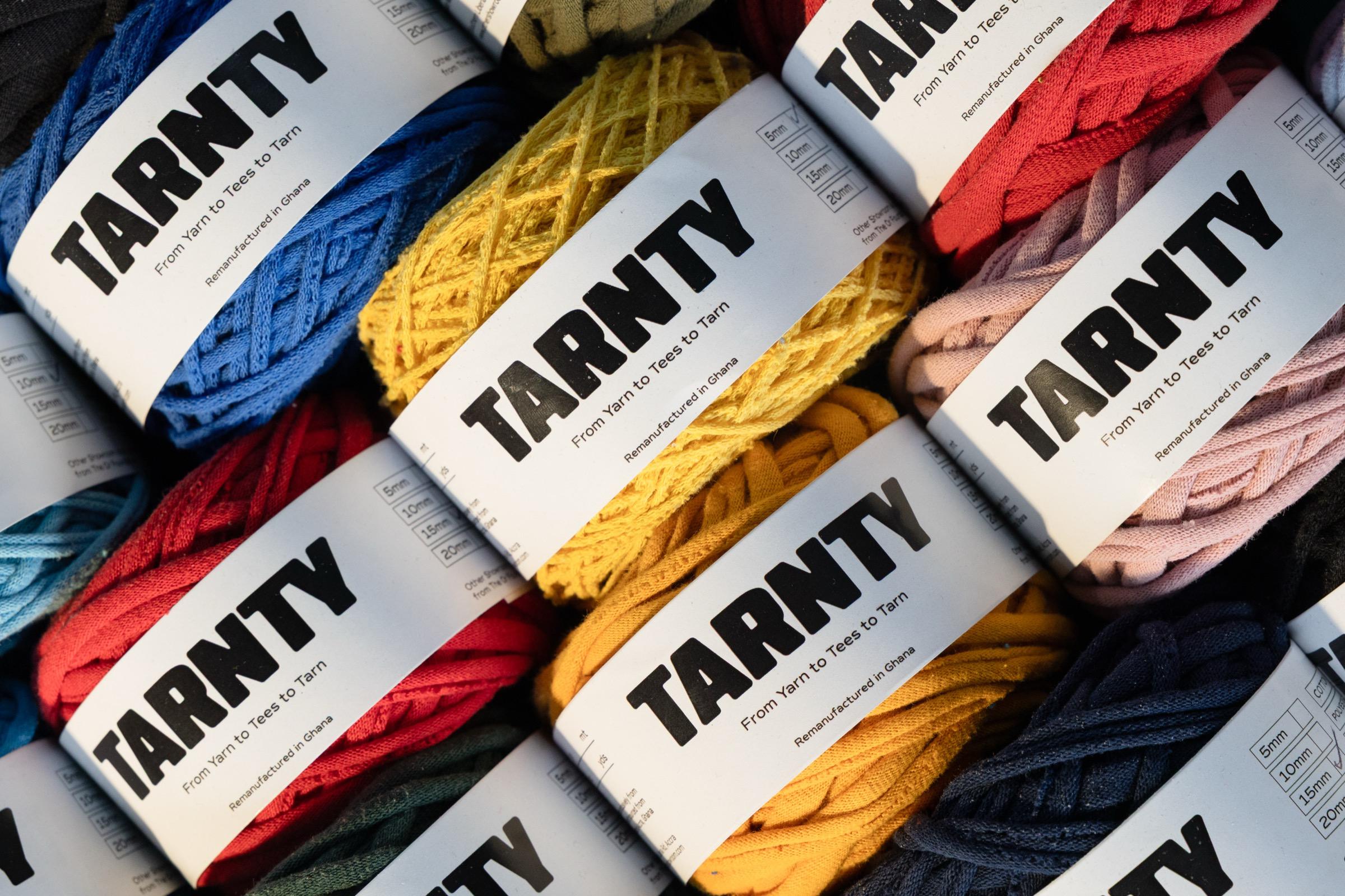 Balls of Tarnty t-shirt yarn in red, blue, yellow and pink, each wrapped in a paper band reading 'From Yarn to Tees to Tarn'.
